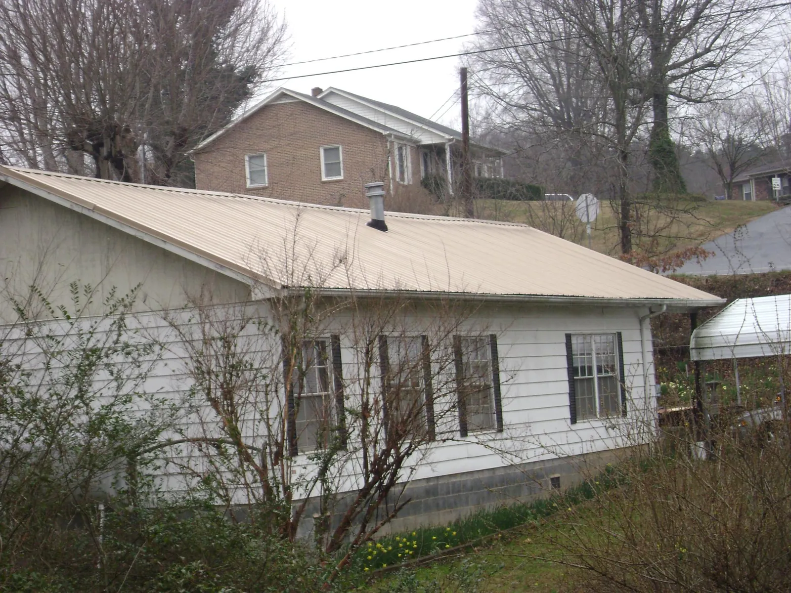 Tan metal roof on a white sided house set into a hillside — Commercial Roofing by Roofing Brothers in Hillsboro